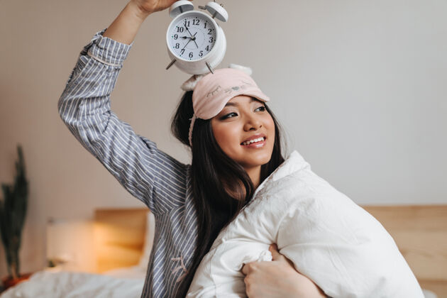睡眠面具穿着条纹睡衣拿着巨大的白色闹钟的女人睡眠魅力健康