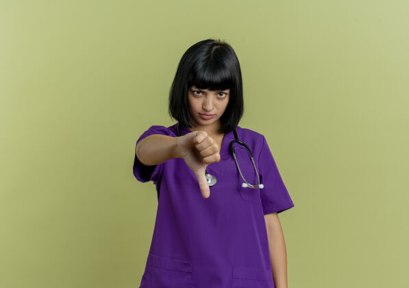 复制年轻的黑发女医生穿着制服 听诊器大拇指朝下 橄榄绿背景 留有复印空间不愉快黑发年轻