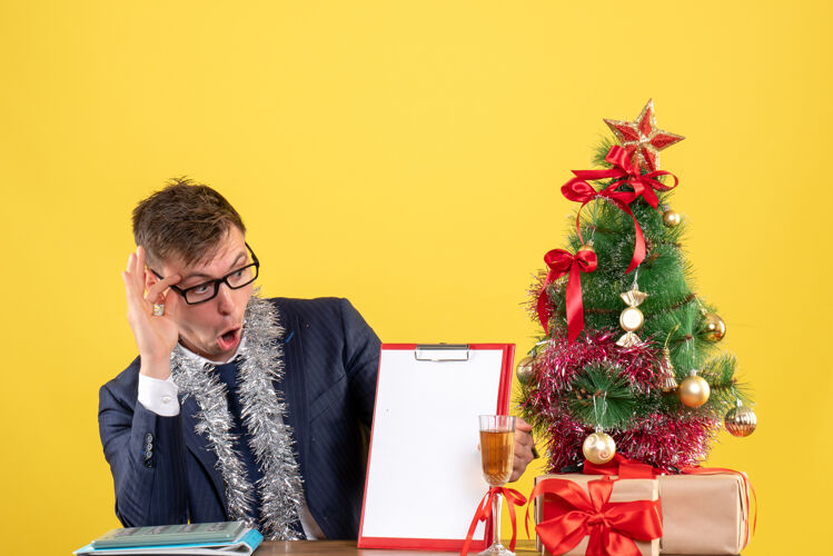 生意人前视图商务人士检查文件坐在圣诞树附近的桌子和黄色背景上的介绍行政人员桌子办公室