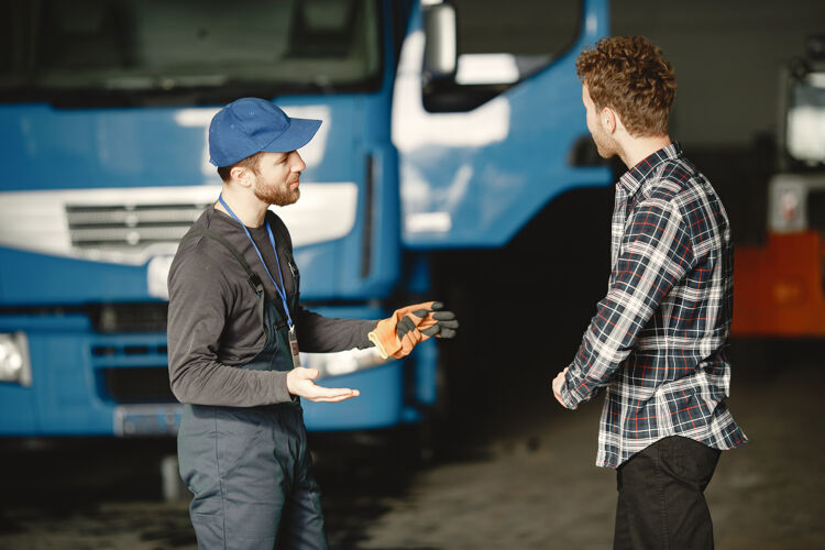 年轻人两个家伙在谈论工作在卡车附近的车库工作用货物转移文件专业车辆制服