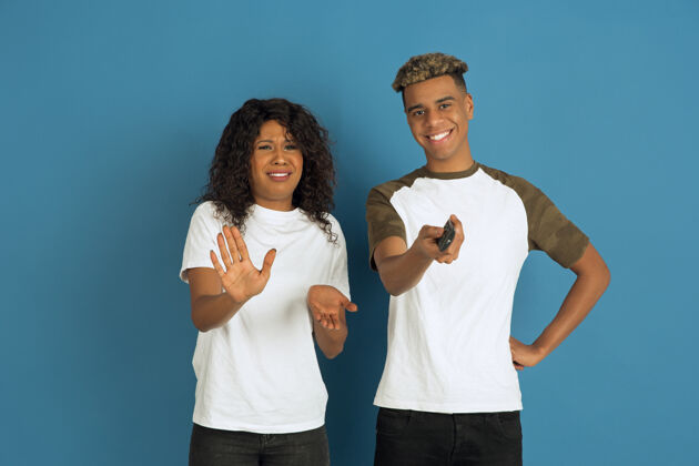 休闲年轻感性的非裔美国人 穿着白色休闲服 在蓝色背景上摆姿势美丽的情侣人类情感的概念 面部表情 关系 广告一起看电视男性金融化妆品