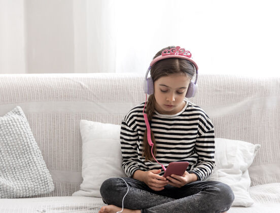 孩子一个可爱的小女孩坐在家里的沙发上 用耳机听音乐房子青少年爱好
