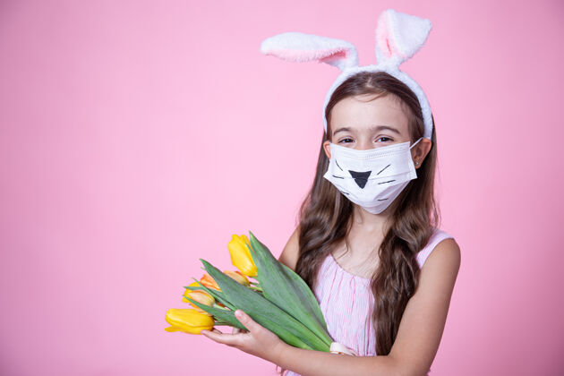 郁金香一个戴着医学面罩的复活节兔子耳朵的小女孩手里拿着一束郁金香 背景是粉色的工作室流行病流行病摄影棚