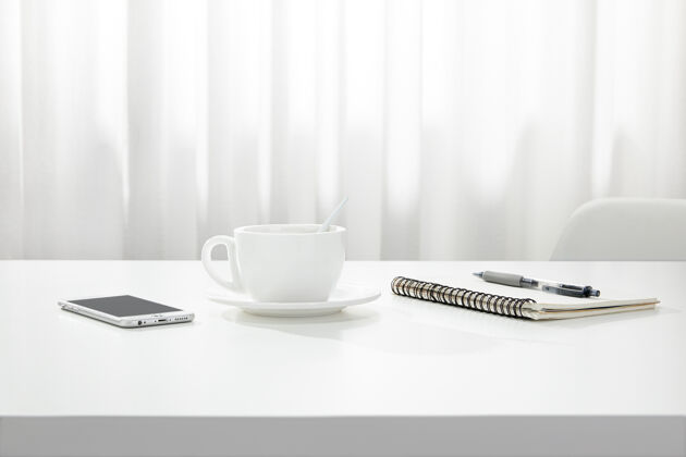 特写一杯咖啡 一本笔记本和一支笔 一部智能手机的特写镜头放在一张白色的书桌上 在室内纸张工作作业