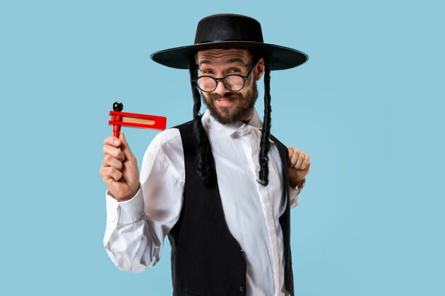 祈祷一个年轻的东正教犹太男子与木制棘轮在节日普瑞姆画像节日 庆祝 犹太教 传统 宗教概念滑稽帽子传统