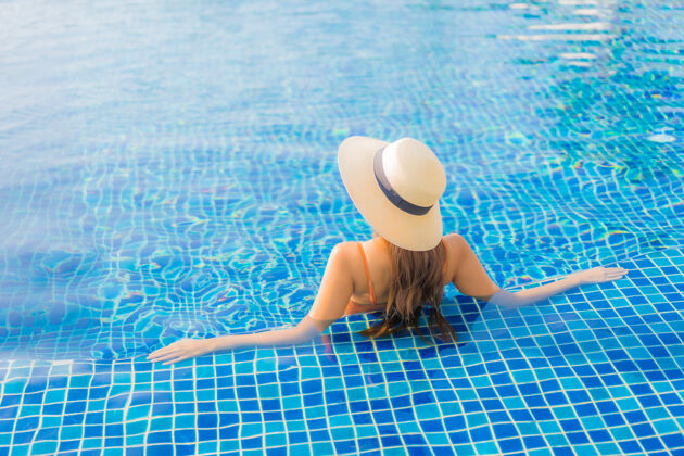 游泳池肖像美丽的亚洲年轻女子放松微笑休闲周围的室外游泳池在度假酒店海景亚洲人水疗健康