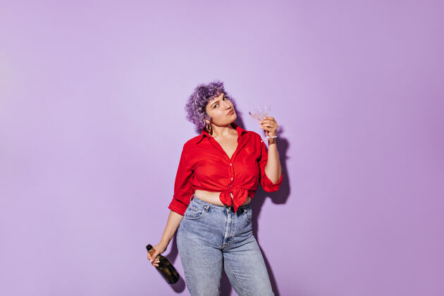 时尚穿着红色时髦衬衫的可爱漂亮女人手里拿着玻璃杯和一瓶白葡萄酒 还有淡紫色肖像紫色太阳镜