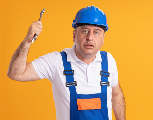 人焦虑的成年建筑工人穿着制服 手里拿着隔离在橙色墙上的扳手公民焦虑建设者