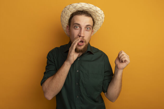 帅哥一个戴着沙滩帽的金发帅哥惊讶地把手放在嘴边 指着身后的橘黄色墙壁站举行点