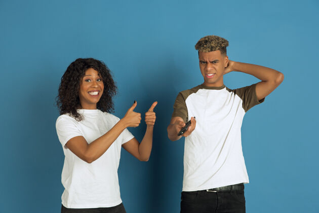 表情年轻感性的非裔美国人男女在蓝色背景上摆姿势美丽的情侣人类情感的概念 面部表情 关系 广告一起看电视 她最喜欢的频道年轻广告人类