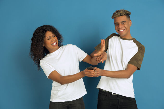 年轻年轻感性的非裔美国人男女在蓝色背景上摆姿势美丽的情侣人类情感的概念 面部表情 关系 广告一起看电视 他最喜欢的频道女孩姿势朋友