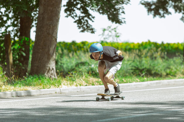 危险在阳光明媚的日子里 在草地附近玩滑板的人穿着装备的年轻人在沥青路面上骑马和玩长板休闲活动 运动 极限 爱好和运动的概念锻炼年轻技巧