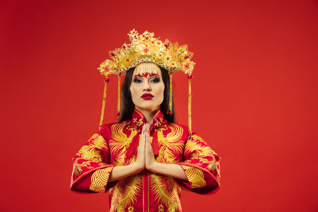 服装中国传统的优雅女子在摄影棚的红色背景美丽的女孩穿着民族服装中国新年 优雅 优雅 表演者 表演 舞蹈 女演员 服装的概念肖像新年轻人