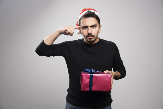 圣诞老人一个愤怒的男人拿着一个礼品盒在灰色的墙上模特礼物肖像