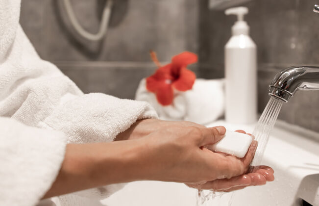 手一个穿着晨衣的女人在自来水下用肥皂洗手水龙头肥皂浴室