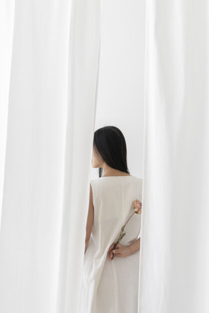 隐藏一个亚洲女人手里拿着一朵粉色的牡丹花在白色的窗帘中间干花后方织物