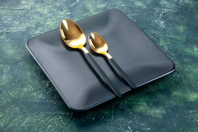 黑色方盘子前视图黑色方形板与金色勺子在黑暗的背景厨房晚餐深色