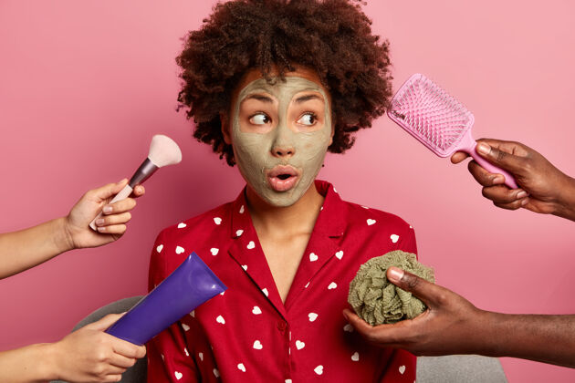 皮肤Spa 保健概念惊讶的黑人年轻女子戴着泥质面膜 一边看一边 穿上国产睡衣 去梳头面部护理粘土美国