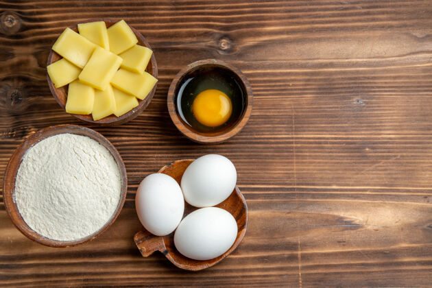 灰尘俯视整个生鸡蛋与面粉和奶酪在棕色的桌子上鸡蛋面团面团面粉灰尘鸡蛋视图面团