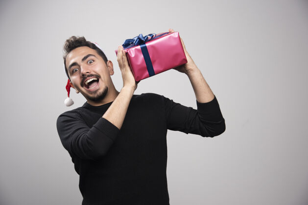 姿势一个年轻人拿着一个礼品盒在灰色的墙上模特圣诞男人