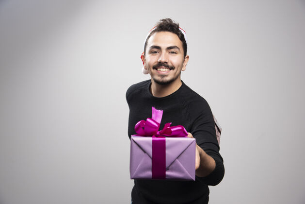 男孩一个年轻人拿着一个礼品盒在灰色的墙上盒子礼物男人