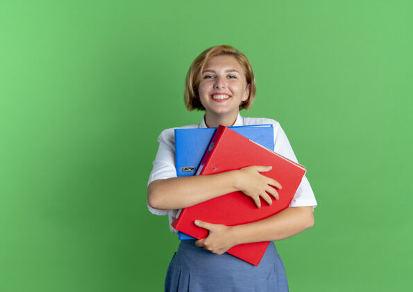 金发年轻的笑容可掬的金发俄罗斯女孩拿着文件夹隔离在绿色背景与复制空间俄罗斯年轻持有