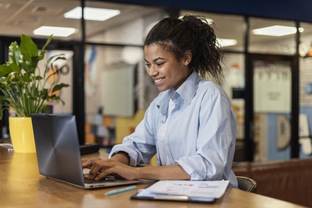 会议笑脸女人在办公室里用笔记本电脑工作的侧视图办公室工作水平