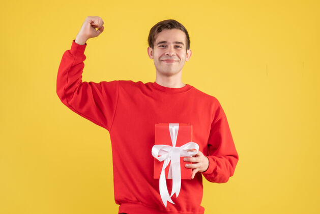 人物正面图：穿着红色毛衣的年轻人拿着礼物放在黄色背景的复印处成人人物快乐