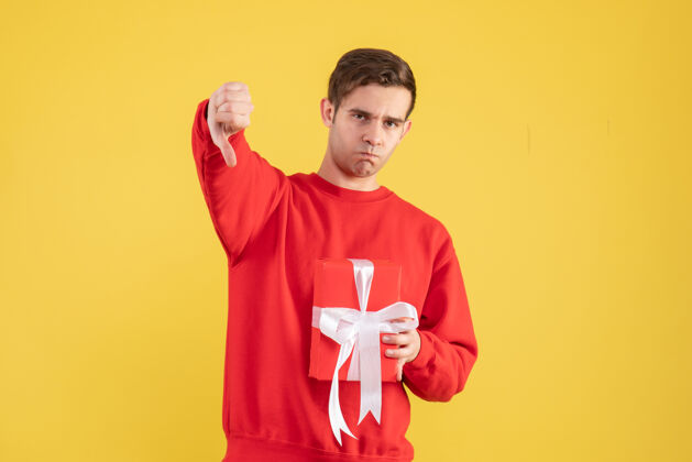 帅哥正面图穿红色毛衣的年轻人在黄色背景上做拇指朝下的标志红色背景拇指