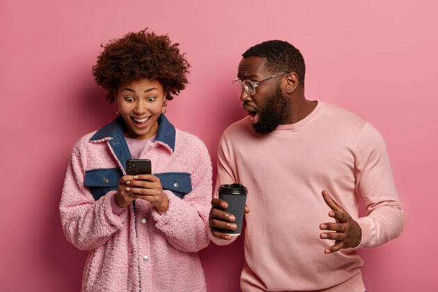 套头衫情绪激动的黑人男女盯着智能手机设备 对惊人的新闻做出反应 收到信息 喝外卖咖啡反应惊喜情侣