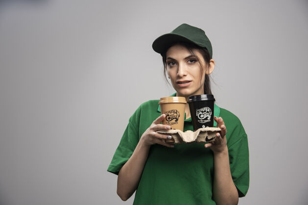 工人穿着绿色制服的女送货员端着咖啡站着事业女性承运人