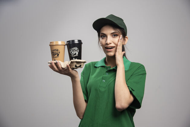 工作穿着绿色制服的女送货员端着咖啡站着快递杯子送货