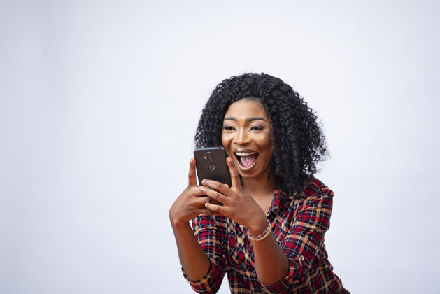 年轻快乐的年轻非洲女性用她的手机和感觉兴奋的东西电话穿着尼日利亚