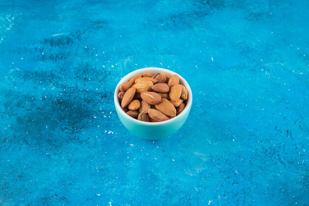 碗在蓝色表面的碗里放着没有壳的杏仁蛋白质美味自然