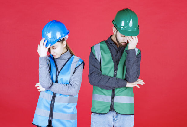 无聊戴着头盔和装备的男女工程师看起来既累又困过度劳累模特姿势