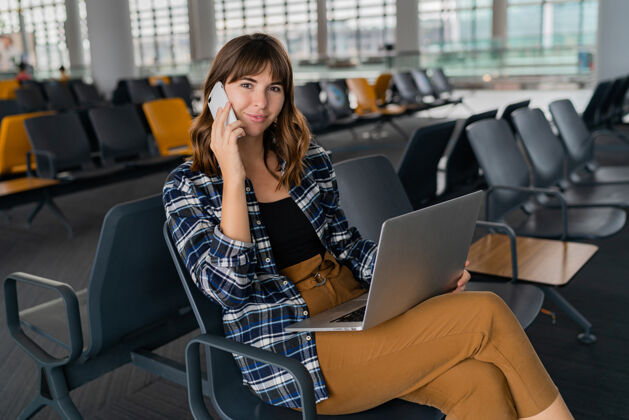 飞行机场年轻女乘客带着智能手机和笔记本电脑坐在候机大厅等待航班旅游年轻笔记本电脑