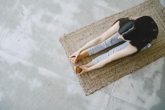 黑发穿着运动服在家沙发和窗户边做瑜伽练习的女孩一健身房冥想