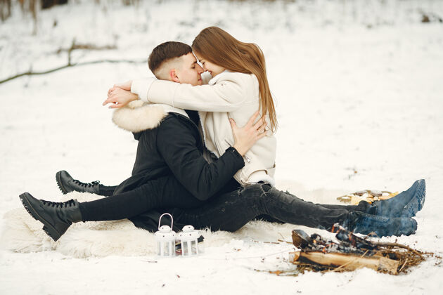 松树生活方式拍摄的一对夫妇在雪林人们在户外度过寒假人们在篝火旁雪成人拥抱