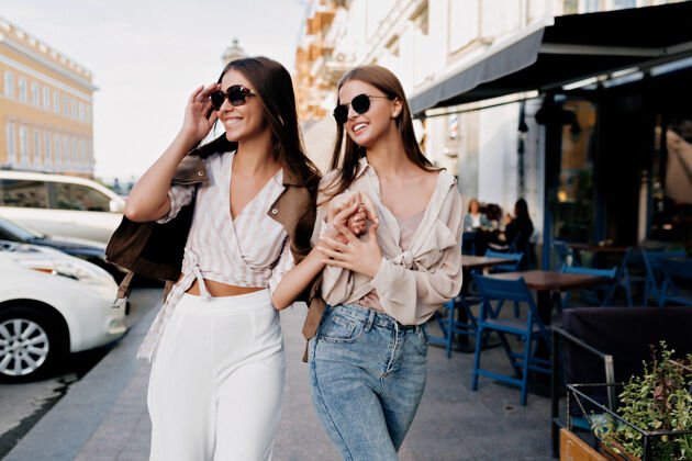积极穿着时髦服装的优雅时尚女性在购物后在城市里嬉戏成人漂亮友谊