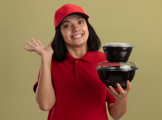 年轻身穿红色制服 头戴鸭舌帽 手举食品包 微笑着挥舞的年轻送货员站在明亮的墙上站着女孩帽子
