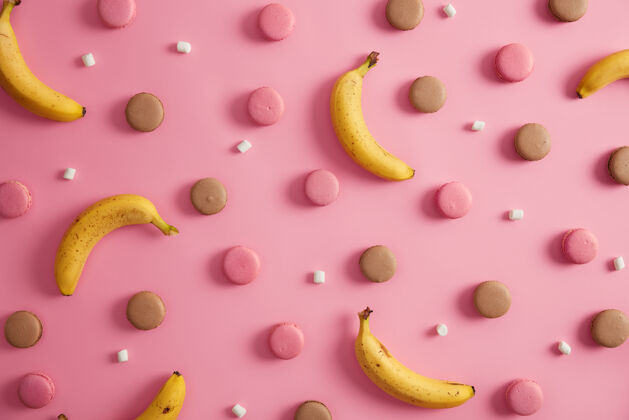 小吃五颜六色的法国甜杏仁饼 白色棉花糖和香蕉 粉色背景不健康的高热量饼干和健康的热带水果您的甜点的想法玫瑰香饼干味道