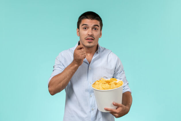 男人正面图：年轻人拿着篮子 手里拿着土豆 在淡蓝色的墙上看电影 孤独的电影院光电影篮子