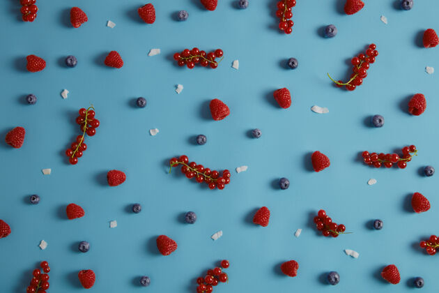 蓝莓上图为美味开胃的成熟浆果 可供食用或制作甜点蓝色背景上有新鲜的覆盆子 红醋栗 蓝莓和椰子片混合水果有利于您的健康营养浆果椰子香草