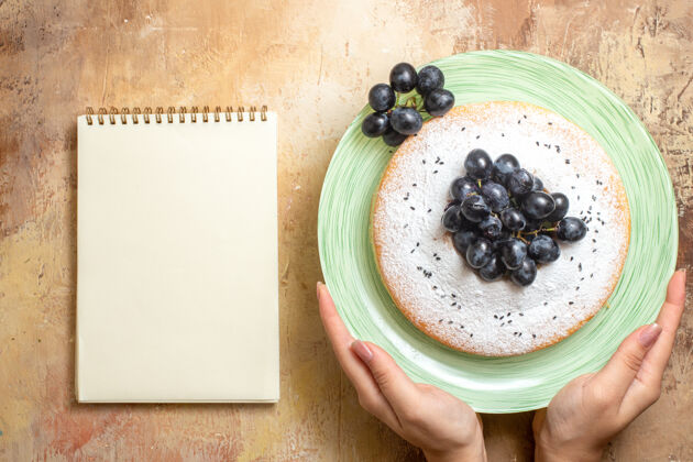 新鲜顶部特写镜头一个蛋糕绿色盘子的开胃蛋糕与葡萄在手笔记本特写蛋糕甜点