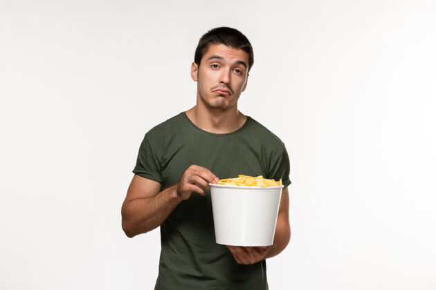 观看正面图：穿着绿色t恤的年轻男性 带着土豆cips 在白墙上看电影电影人男性孤独电影电影院拳击杯子马克杯