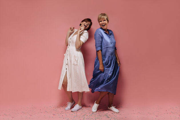 女士两个穿着迷笛夏装 穿着白色运动鞋 留着短发的女人 在孤立的粉色背景下欢笑着女性中年人蓝色