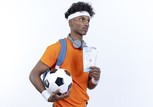 运动看着身边年轻的黑人运动男子戴着头带和腕带拿着球和票隔离在白色背景壁板球腕带