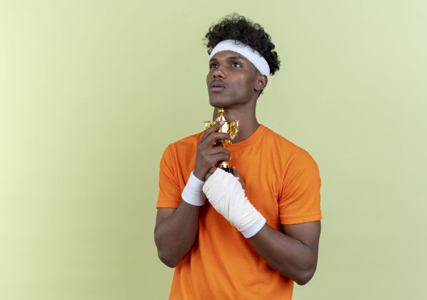 年轻看着年轻的美国黑人运动男子戴着头带和手带与绷带手腕举行杯隔离在绿色背景运动型佩戴头带