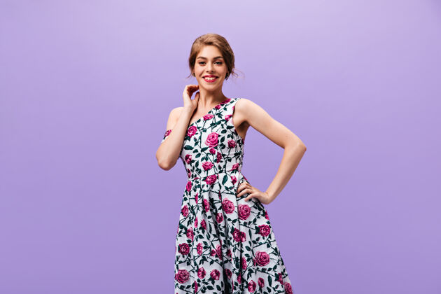 肖像身着时尚连衣裙的积极女士在紫色背景上微笑穿着花式时尚服装的漂亮波浪发女士在镜头前摆姿势女性连衣裙时尚