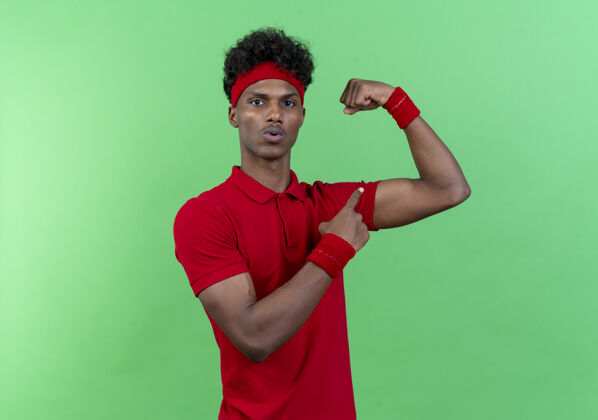 年轻令人印象深刻的年轻美国黑人运动男子戴头带和腕带做强有力的手势和绿色背景孤立点穿着印象非裔美国人